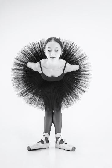 peacock. a ballerina in a black tutu is leaning forward with her arms crossed behind her back