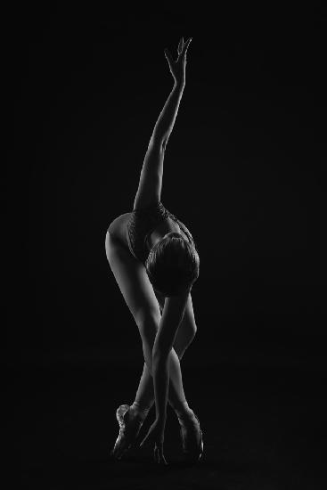 string. the ballerina is standing on pointe shoes leaning forward and wrapping her arm around