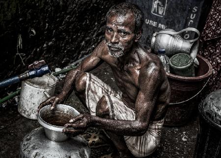 Man filling a pitcher with water in the streets of Bangladesh.